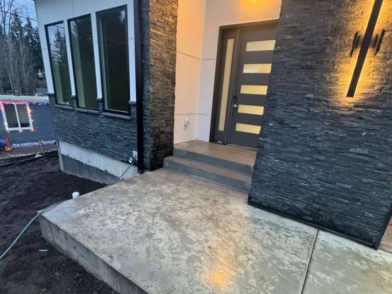 Front entry of the finished Bothell home at dusk: stacked stone columns, modern wood door and warm sconce lighting